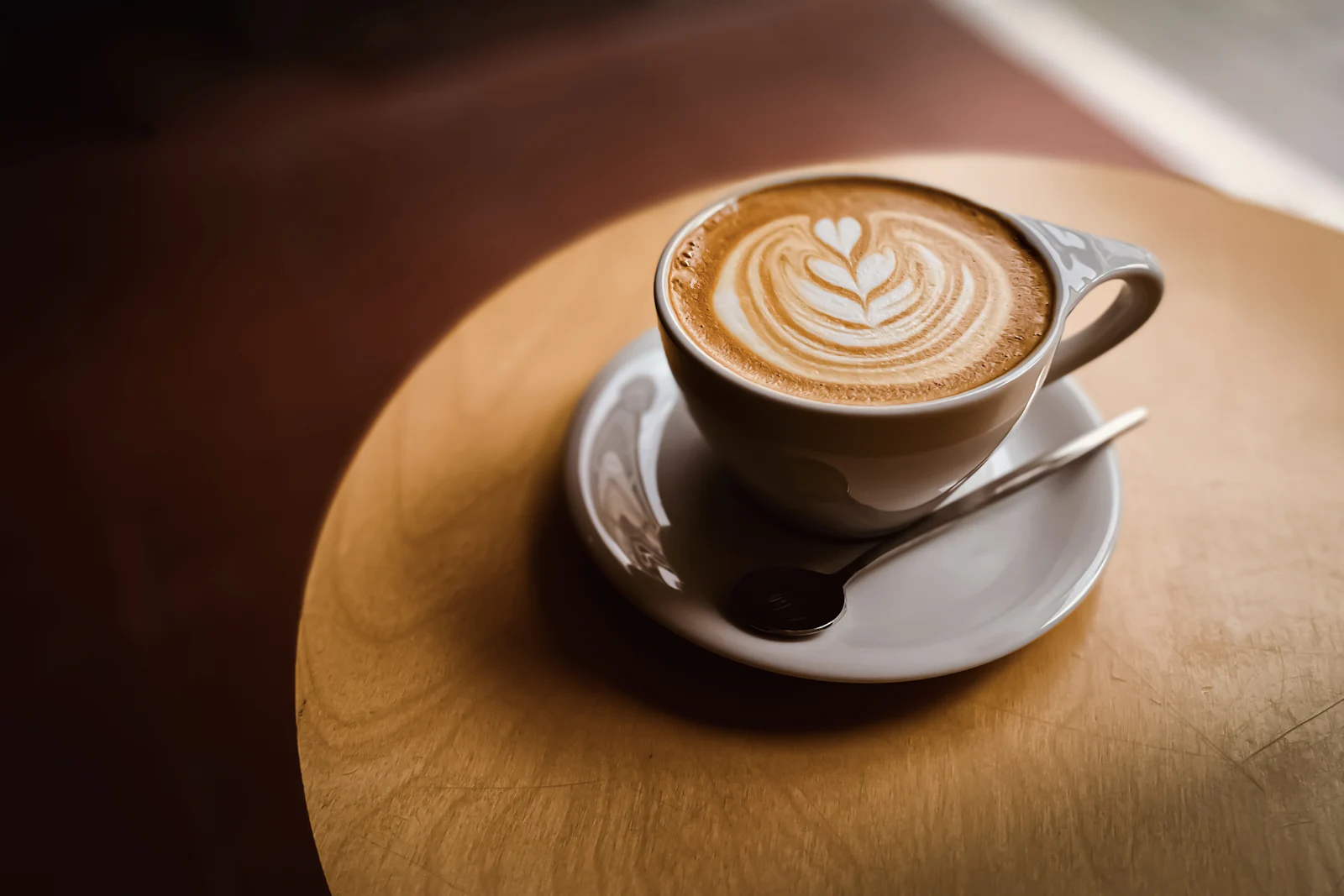 Ceașcă de cappuccino cu latte art pe o farfurioară, pe masă de lemn